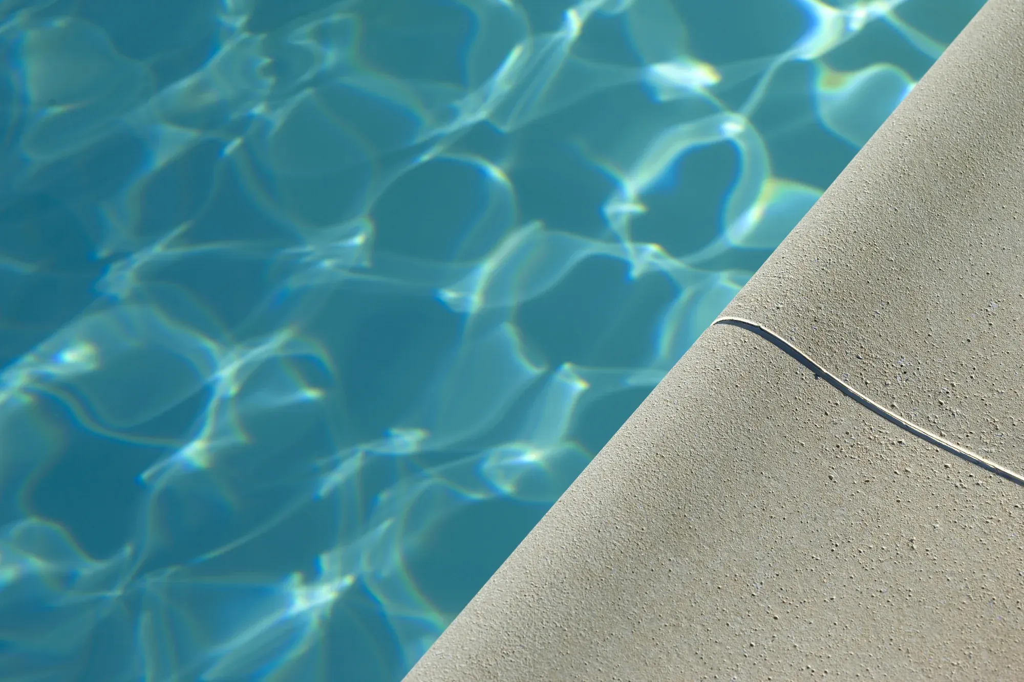 Pool coping edge where the deck meets clear blue water