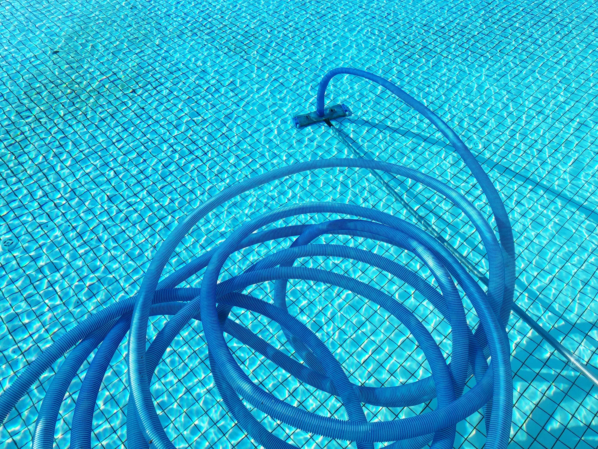 Coiled vacuum hose resting in a mosaic-tiled pool