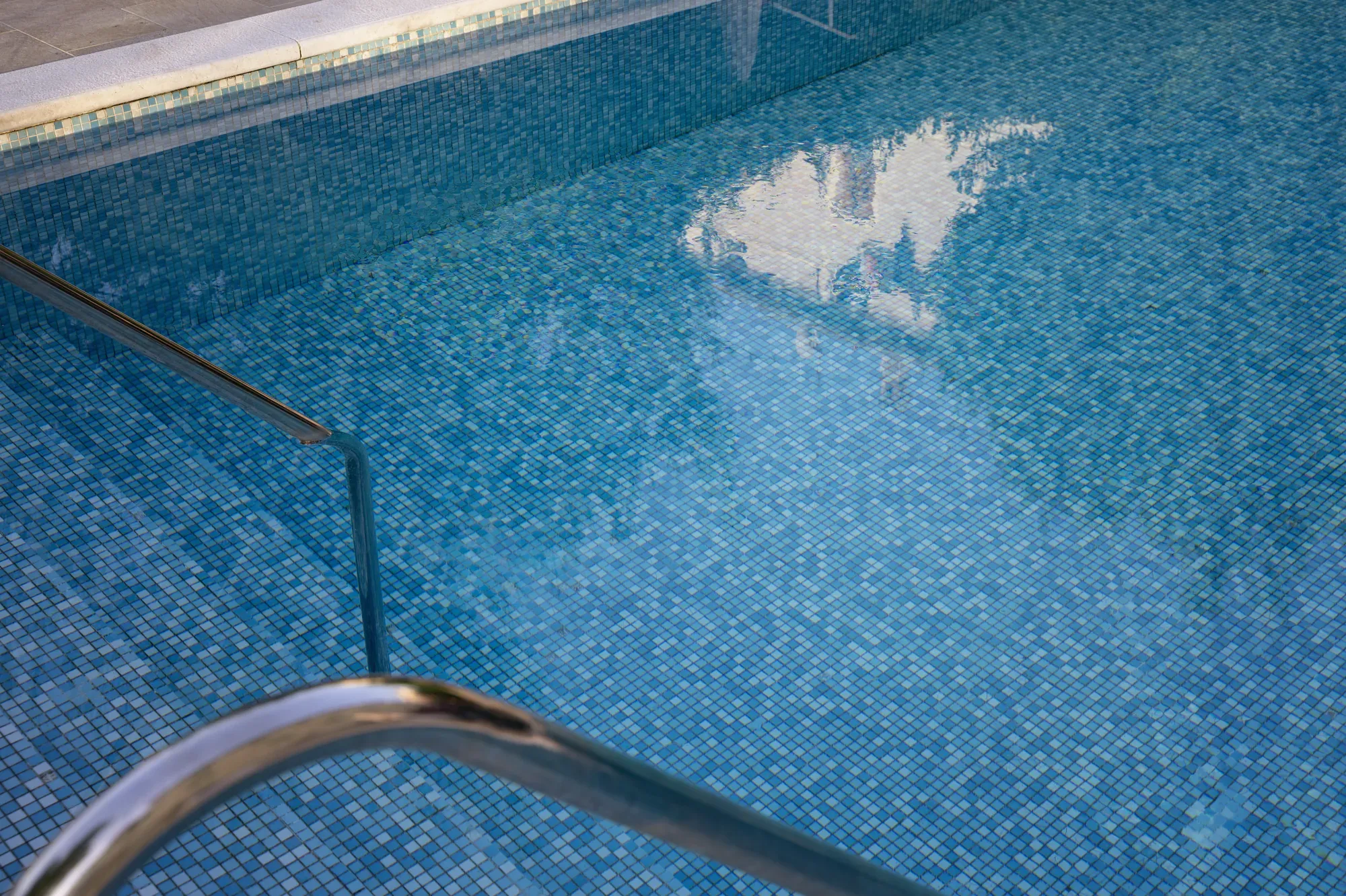 Handrail reflected in the still water of a mosaic-tiled pool