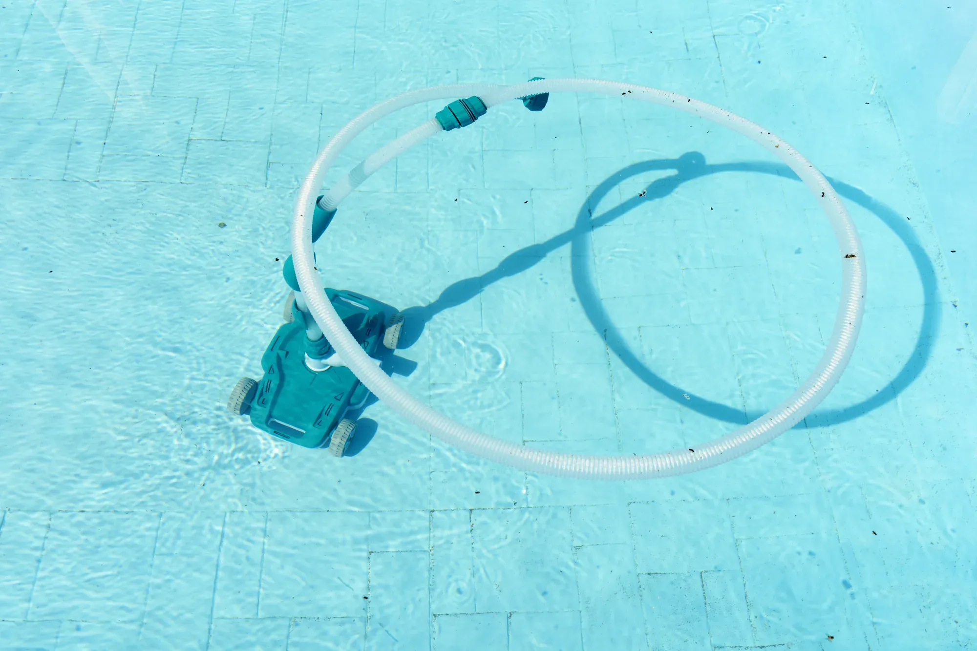 Automatic pool vacuum and its hose coiled on the pool floor