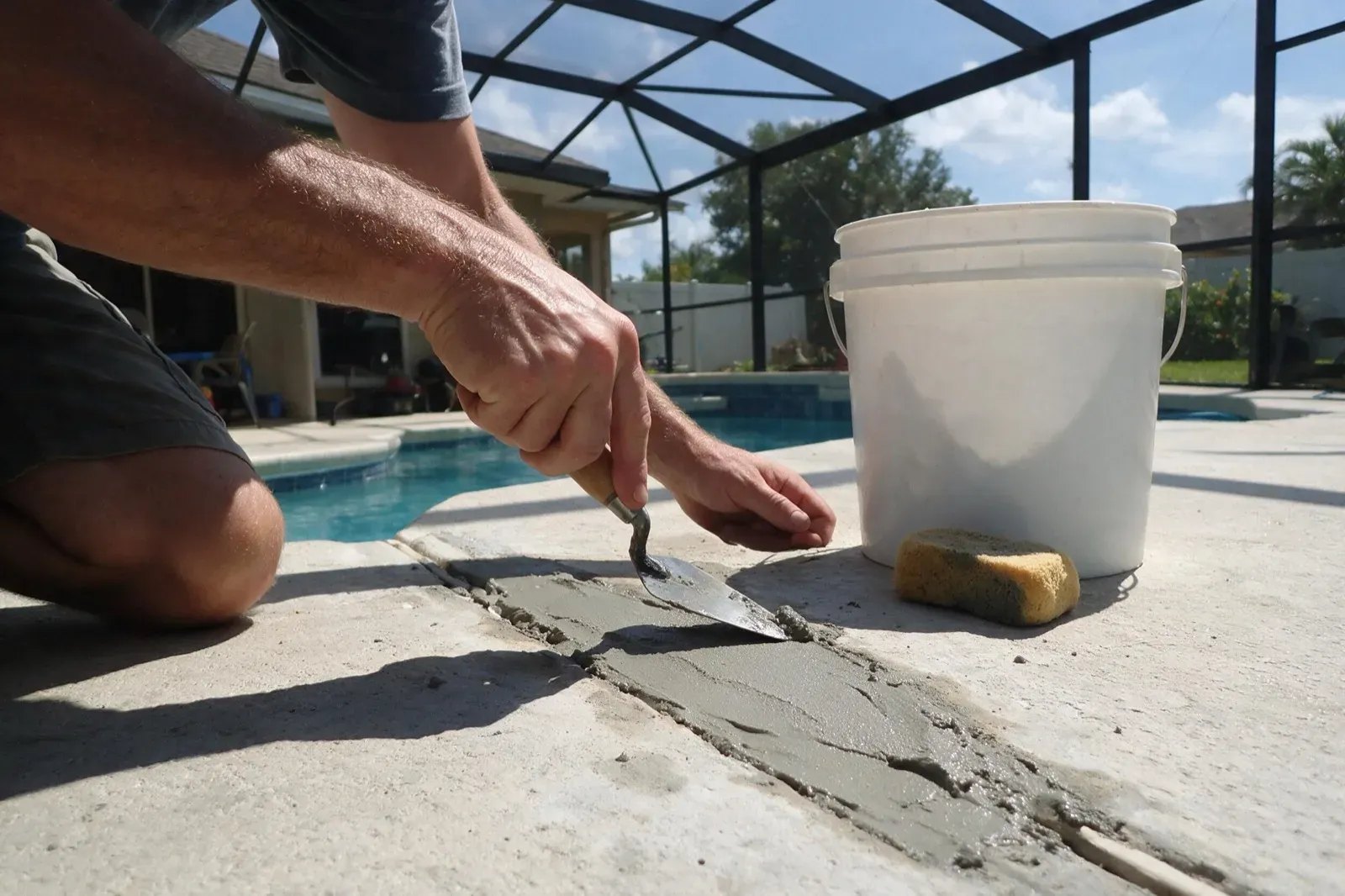 Technician smoothing fresh repair mortar at the pool deck edge